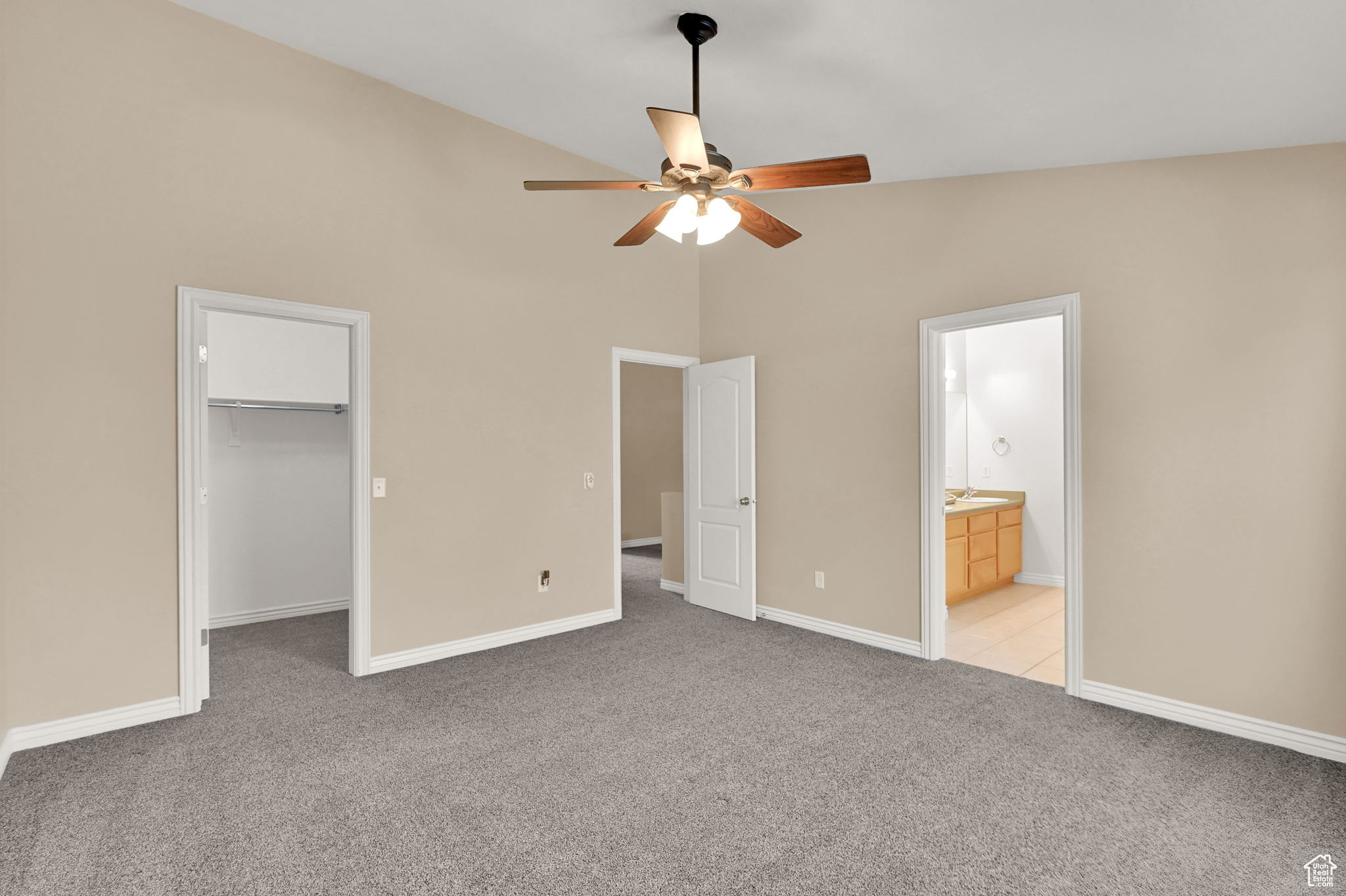 Unfurnished bedroom with a spacious closet, ensuite bath, a closet, light carpet, and ceiling fan