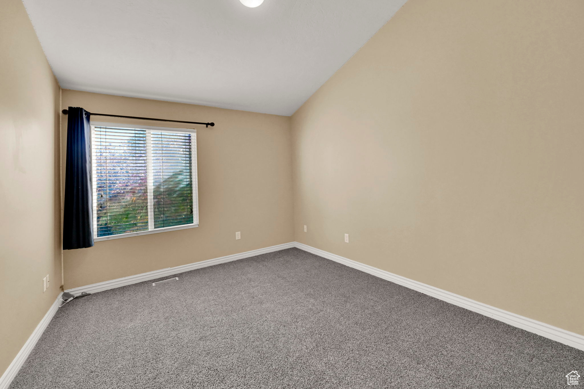 Carpeted empty room featuring vaulted ceiling