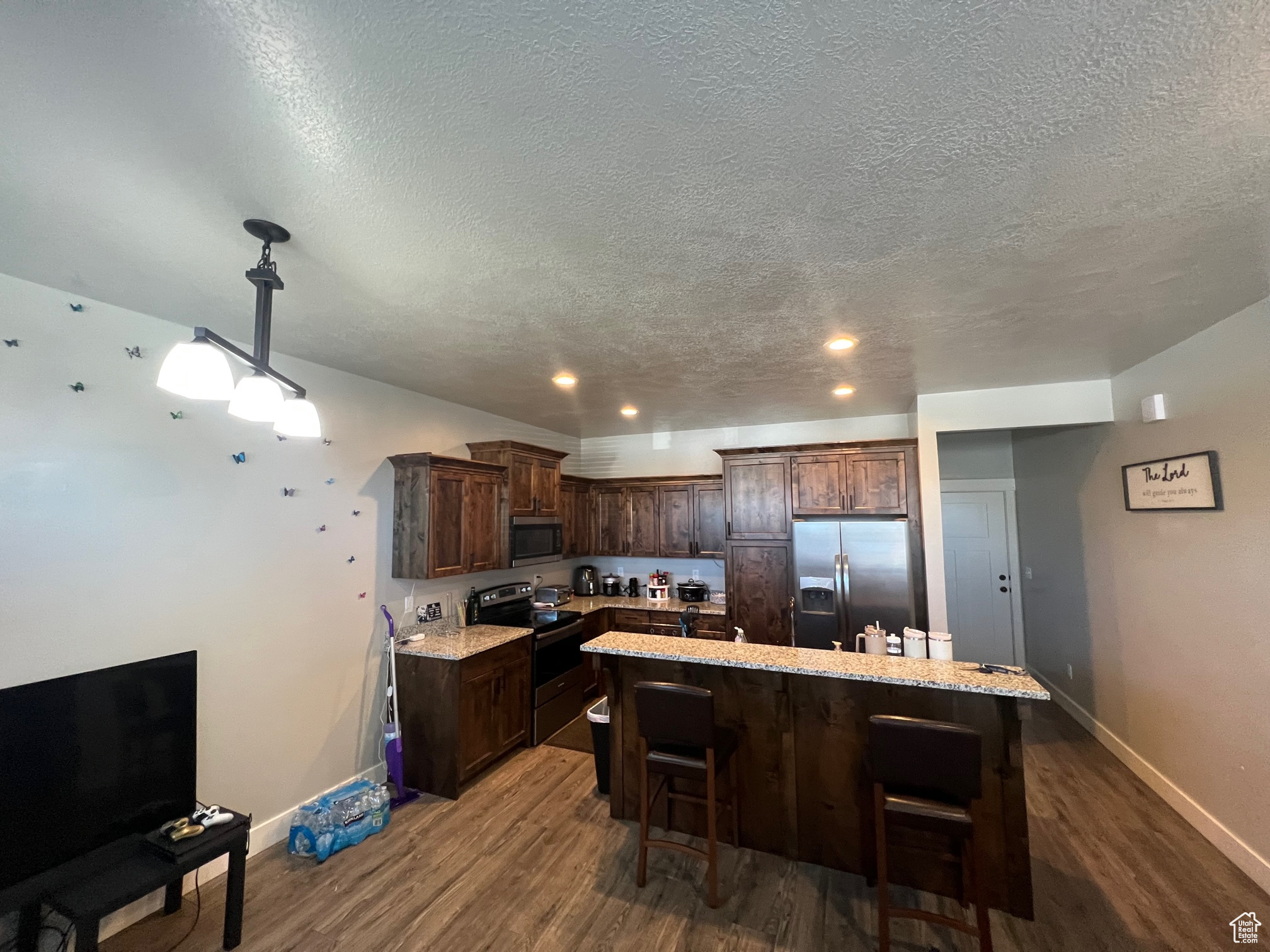 Kitchen featuring stainless steel appliances, decorative light fixtures, a kitchen island, and dark hardwood / wood-style flooring