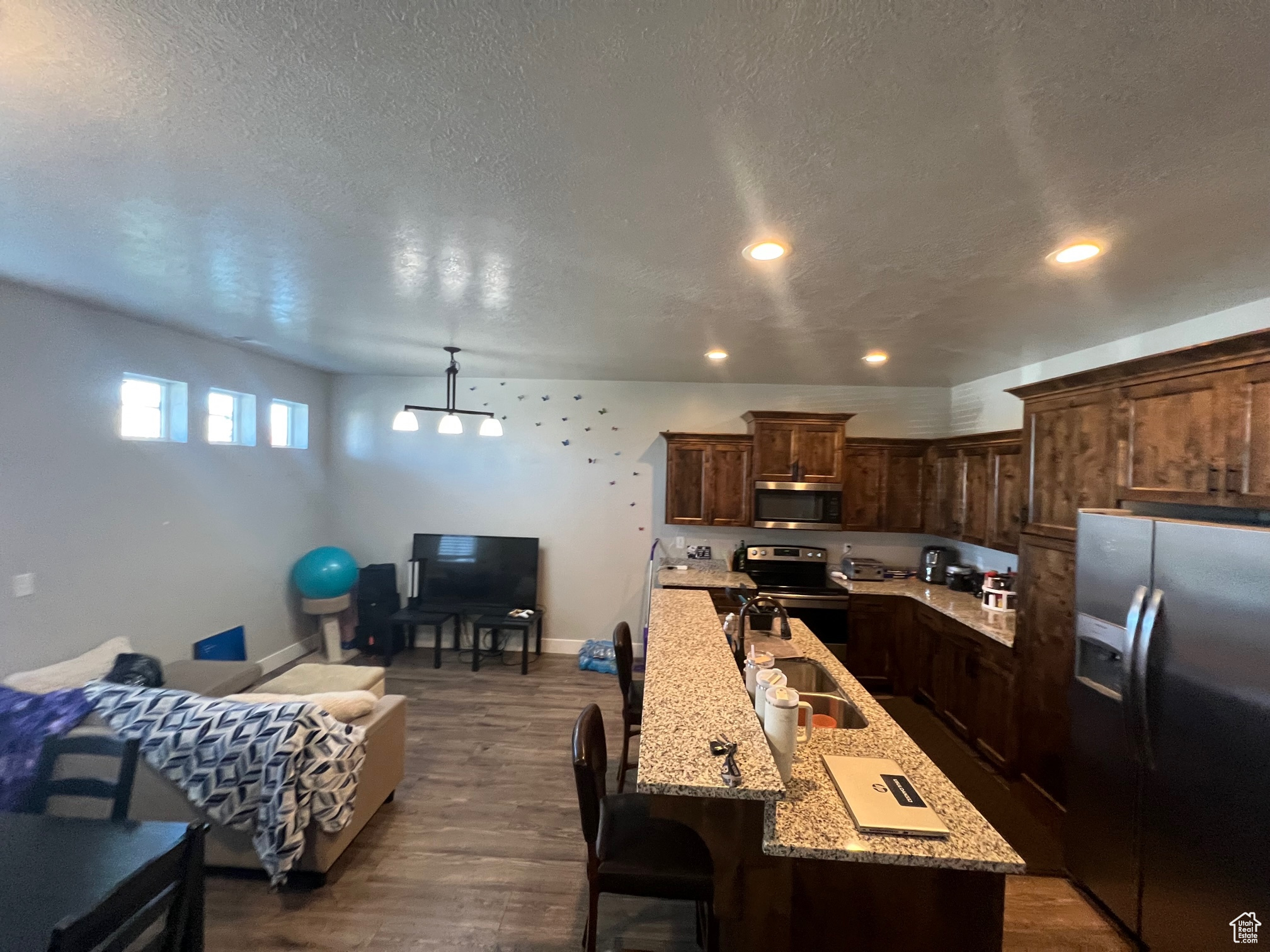 Kitchen with a center island with sink, appliances with stainless steel finishes, light stone countertops, dark wood-type flooring, and dark brown cabinetry