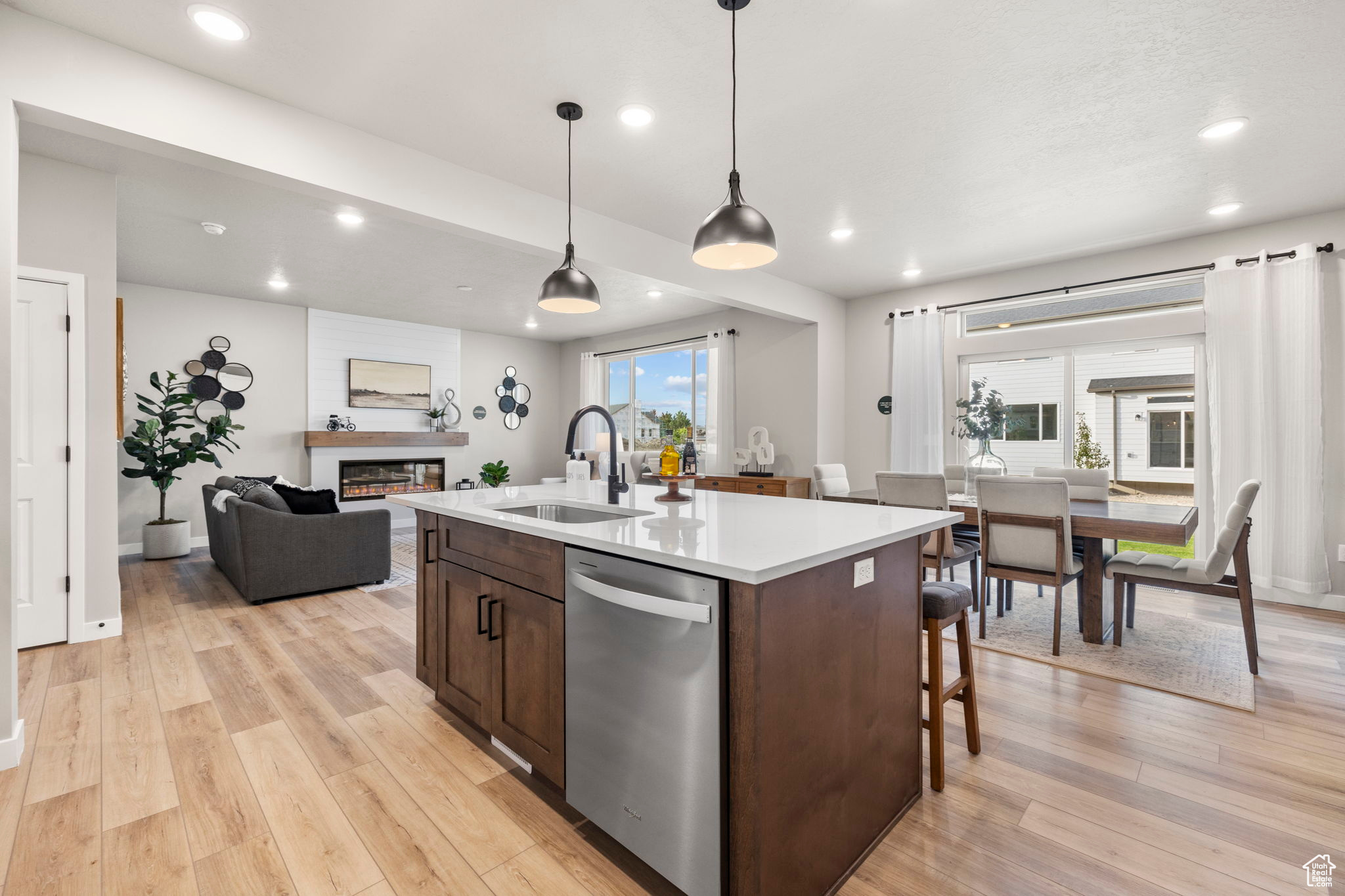 Kitchen featuring light hardwood / wood-style flooring, a wealth of natural light, stainless steel dishwasher, and a kitchen island with sink