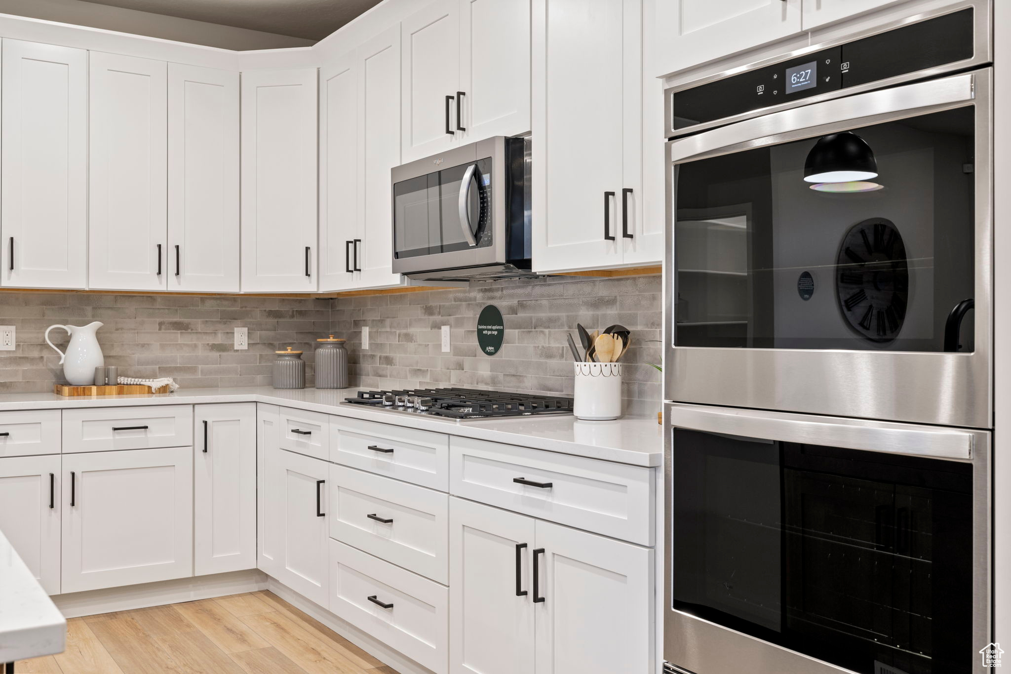 Kitchen with white cabinetry, light hardwood / wood-style floors, appliances with stainless steel finishes, and decorative backsplash