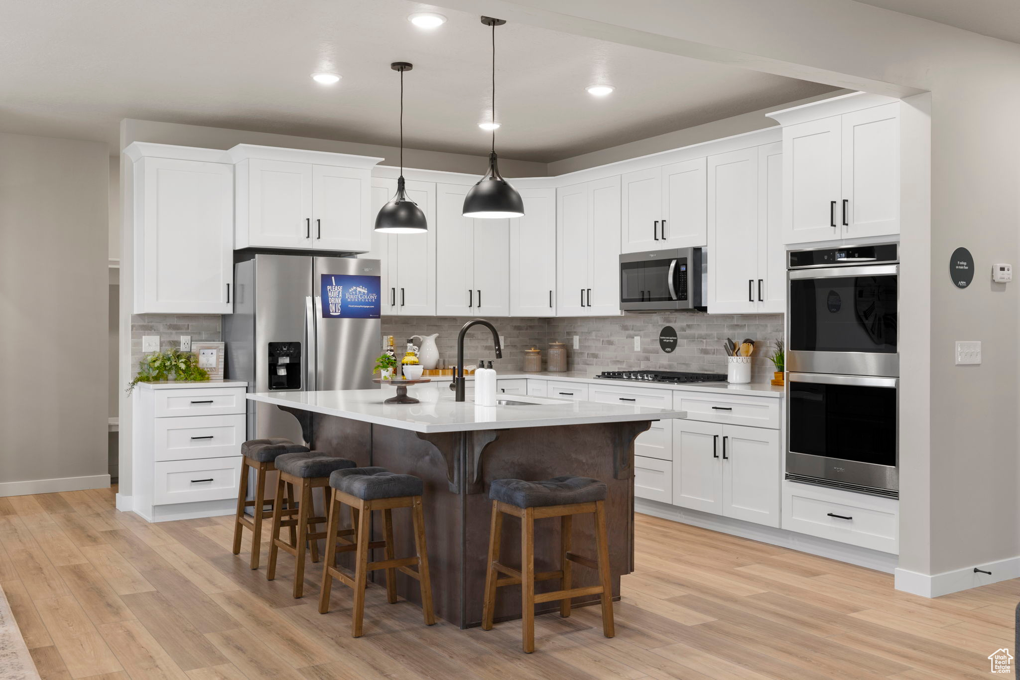 Kitchen featuring sink, pendant lighting, light wood-type flooring, white cabinetry, and appliances with stainless steel finishes