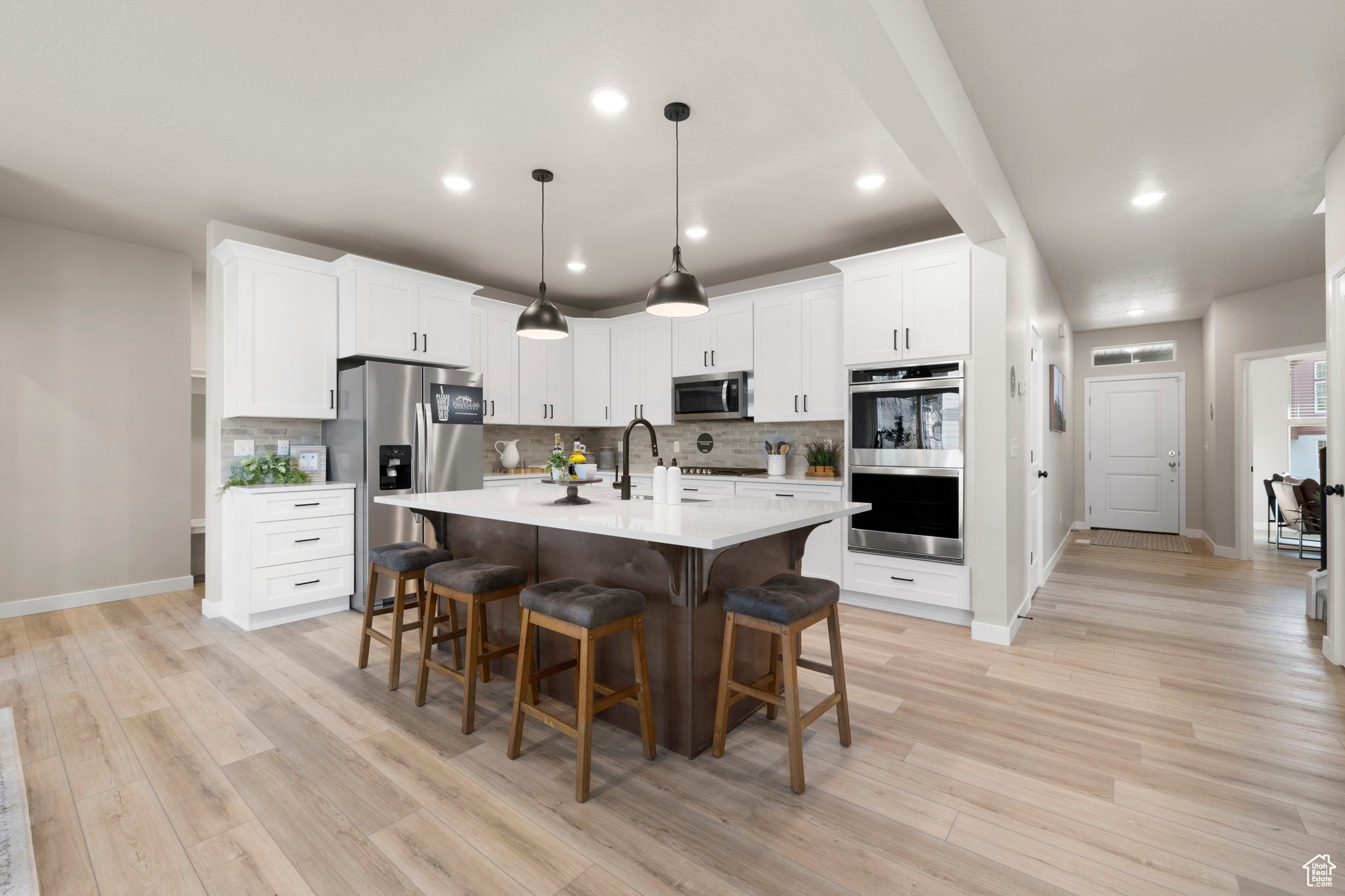 Kitchen featuring stainless steel appliances, light hardwood / wood-style flooring, pendant lighting, and a center island with sink