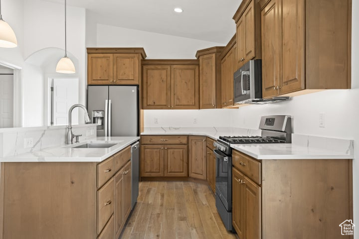 Kitchen featuring stainless steel appliances, sink, vaulted ceiling, decorative light fixtures, and light hardwood / wood-style floors