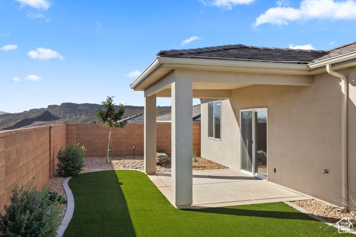 Back of property featuring a mountain view, a patio, and a lawn