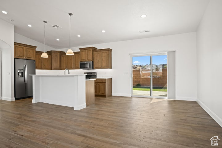 Kitchen with appliances with stainless steel finishes, a center island, dark wood-type flooring, and pendant lighting