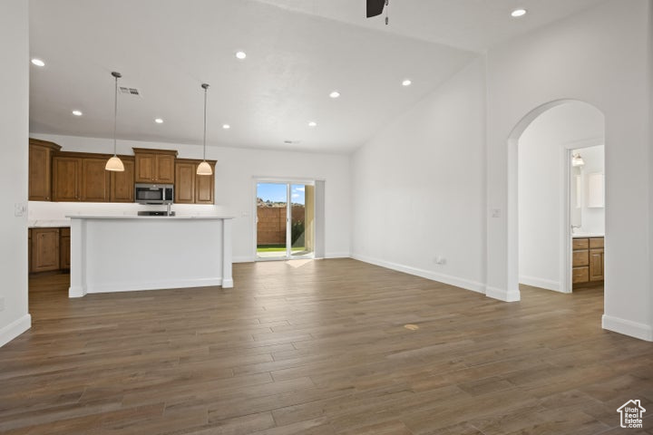 Unfurnished living room with dark wood-type flooring, high vaulted ceiling, and ceiling fan