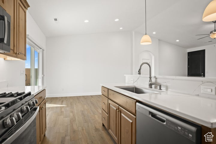 Kitchen with hanging light fixtures, stainless steel appliances, sink, light hardwood / wood-style floors, and ceiling fan