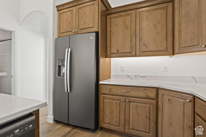 Kitchen featuring dishwasher, light stone counters, light wood-type flooring, and stainless steel fridge with ice dispenser