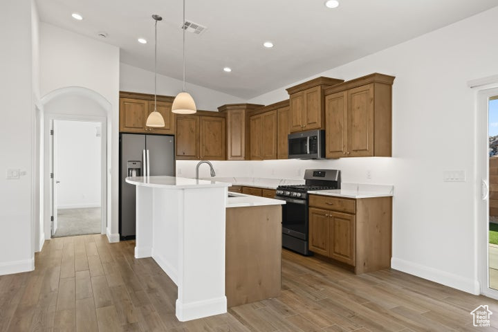 Kitchen featuring appliances with stainless steel finishes, sink, decorative light fixtures, light hardwood / wood-style flooring, and a center island with sink