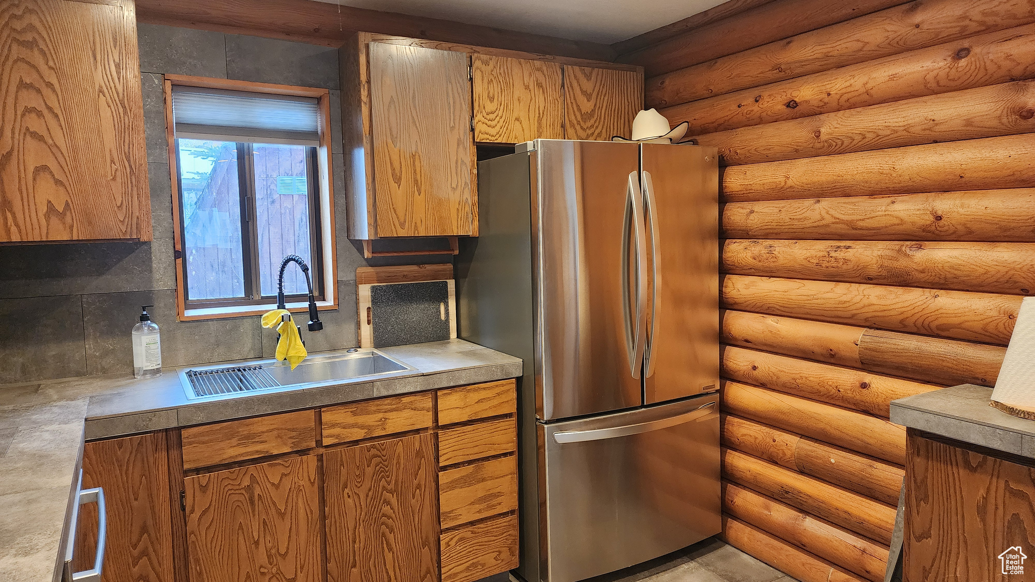 Kitchen featuring log walls, sink, backsplash, and stainless steel refrigerator