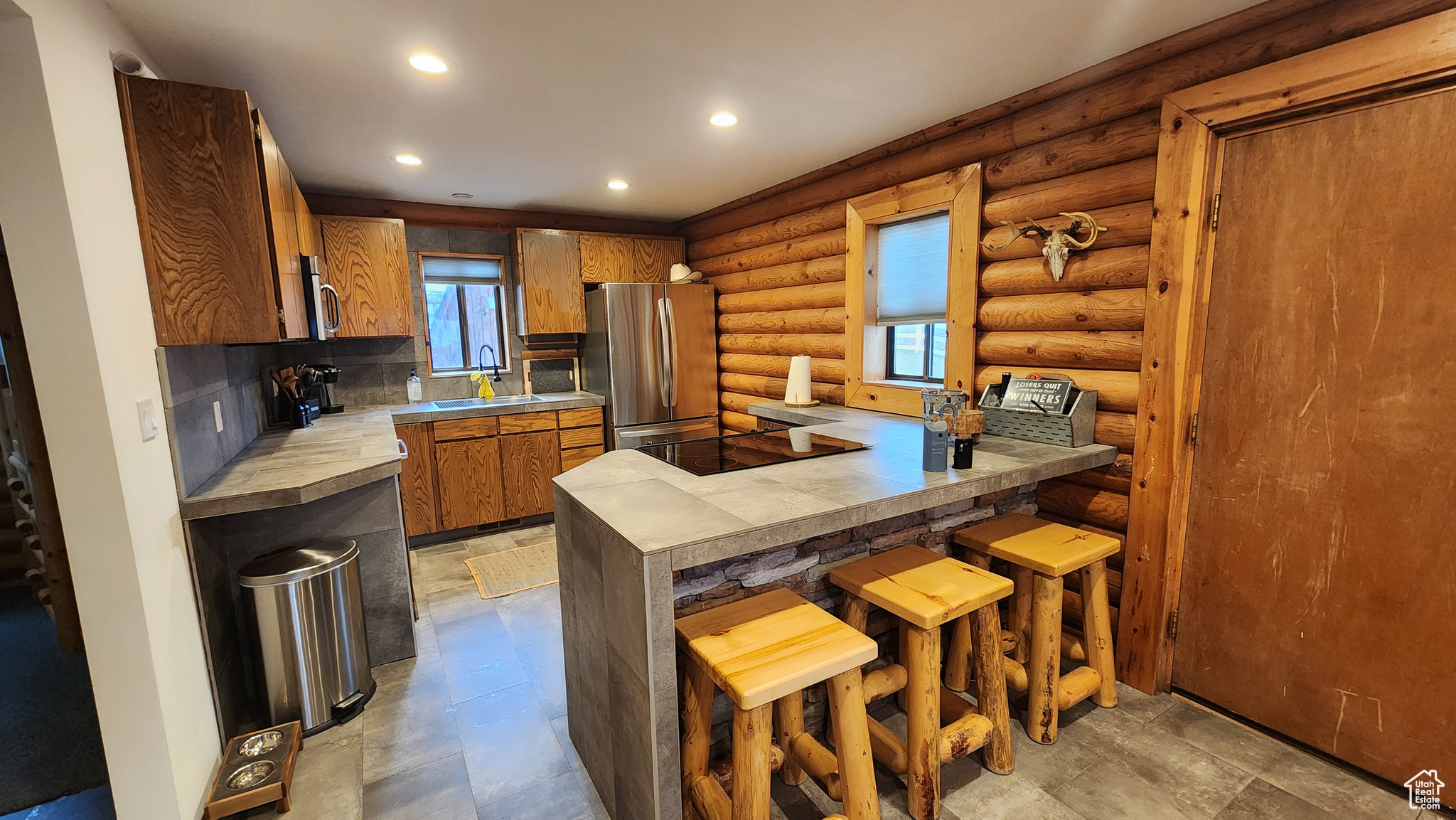 Kitchen featuring a breakfast bar area, kitchen peninsula, sink, log walls, and appliances with stainless steel finishes