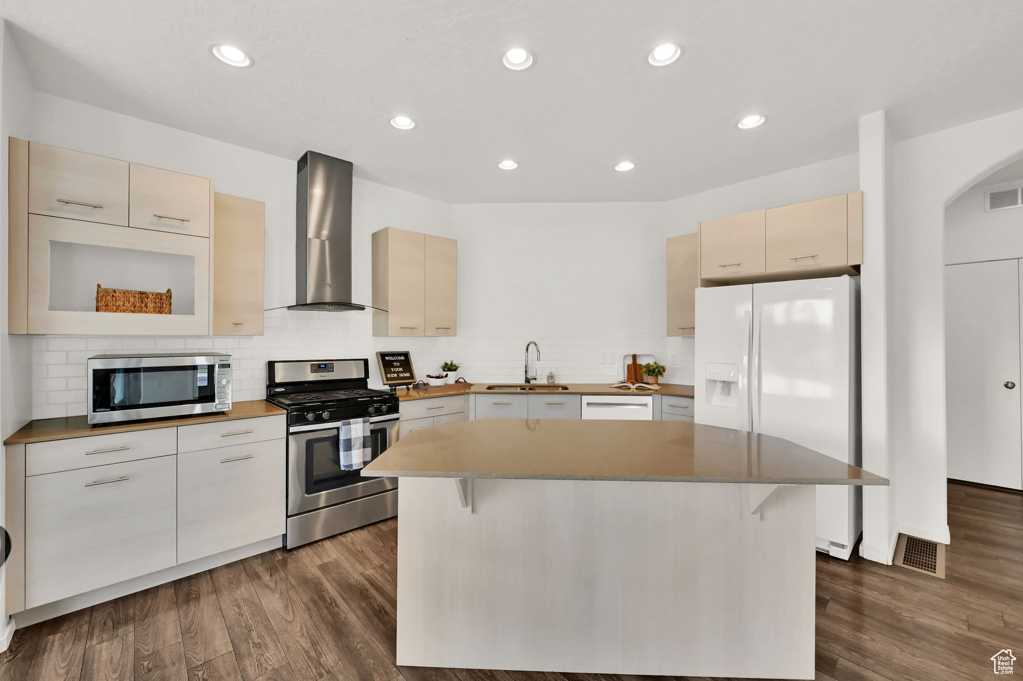 Kitchen featuring dark hardwood / wood-style flooring, stainless steel appliances, sink, wall chimney exhaust hood, and a center island