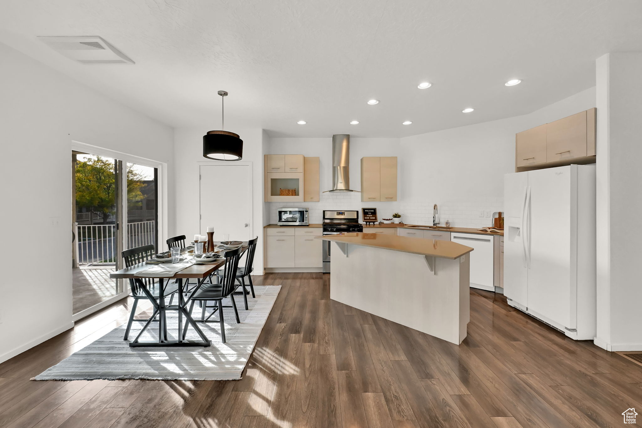 Kitchen with wall chimney range hood, a kitchen island, stainless steel appliances, decorative light fixtures, and dark hardwood / wood-style floors