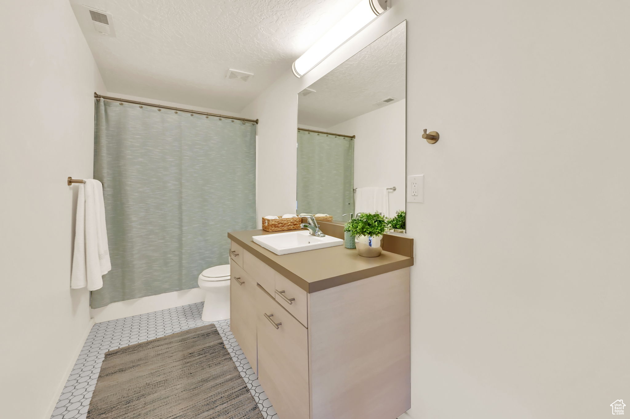 Bathroom with a textured ceiling, toilet, tile patterned floors, walk in shower, and vanity