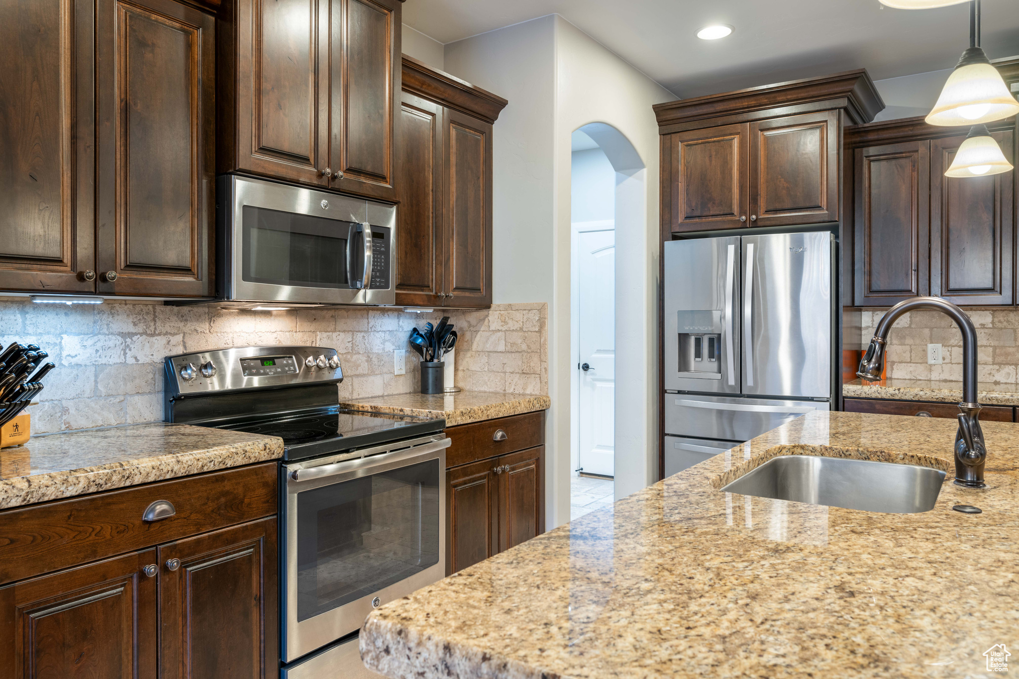 Kitchen with tasteful backsplash, light stone countertops, sink, pendant lighting, and stainless steel appliances