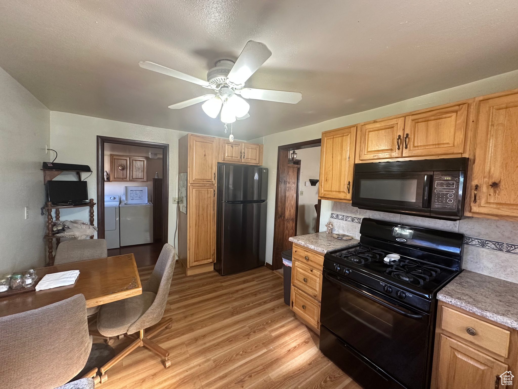 Kitchen featuring independent washer and dryer, backsplash, black appliances, light hardwood / wood-style floors, and ceiling fan