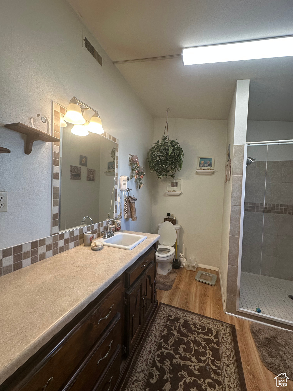 Bathroom with wood-type flooring, toilet, walk in shower, vanity, and decorative backsplash