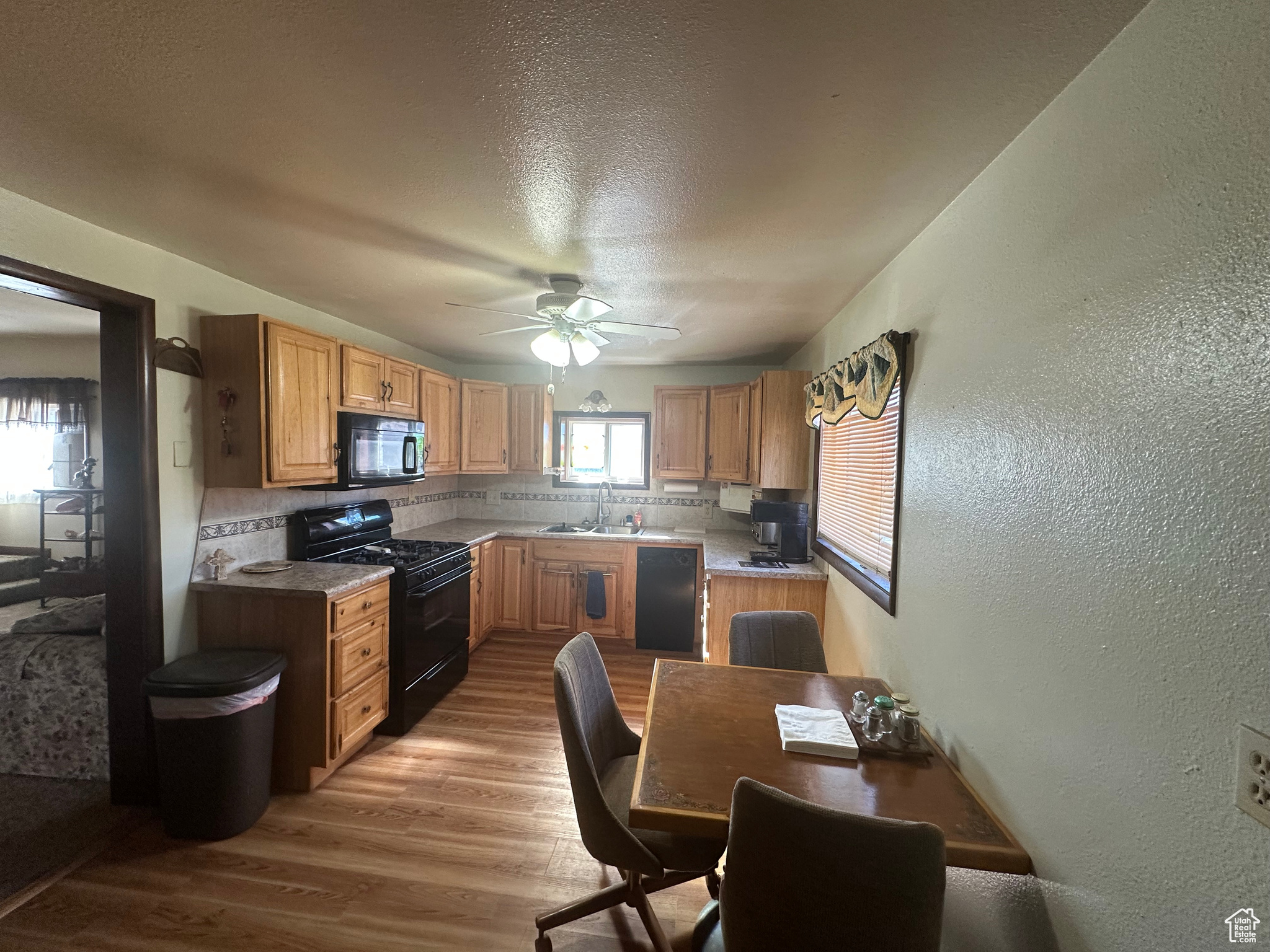 Kitchen with decorative backsplash, ceiling fan, black appliances, light hardwood / wood-style floors, and sink