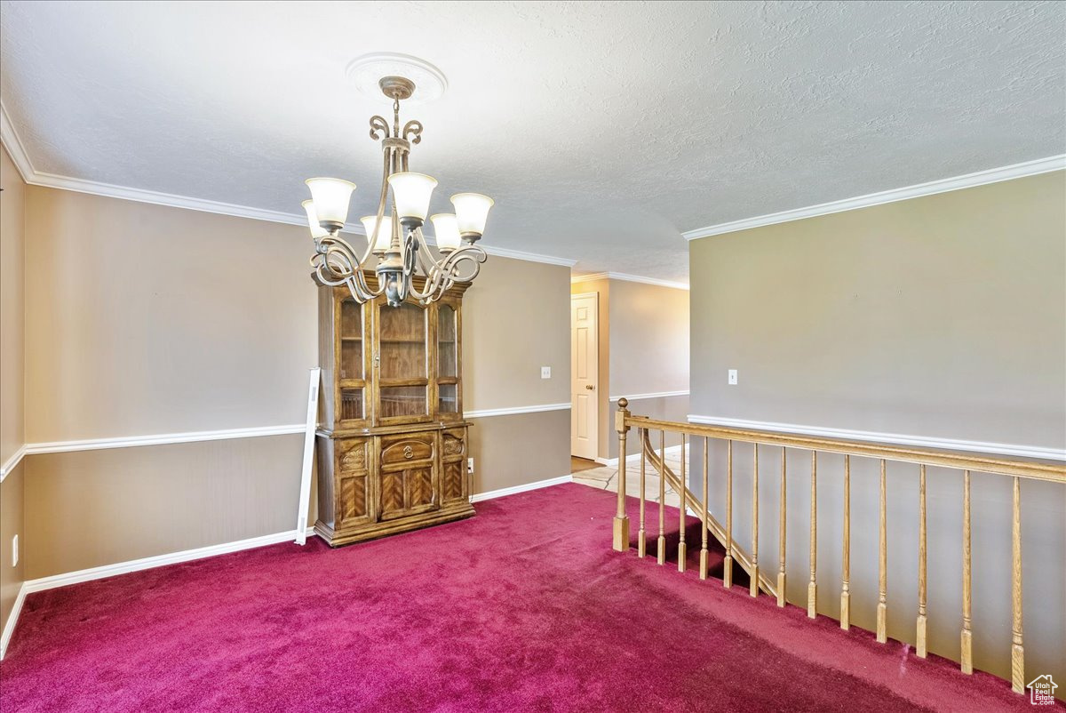 Empty room featuring crown molding, carpet flooring, a textured ceiling, and a chandelier