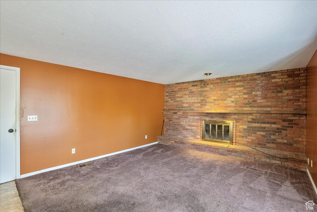 Unfurnished living room featuring a textured ceiling, a fireplace, and carpet floors