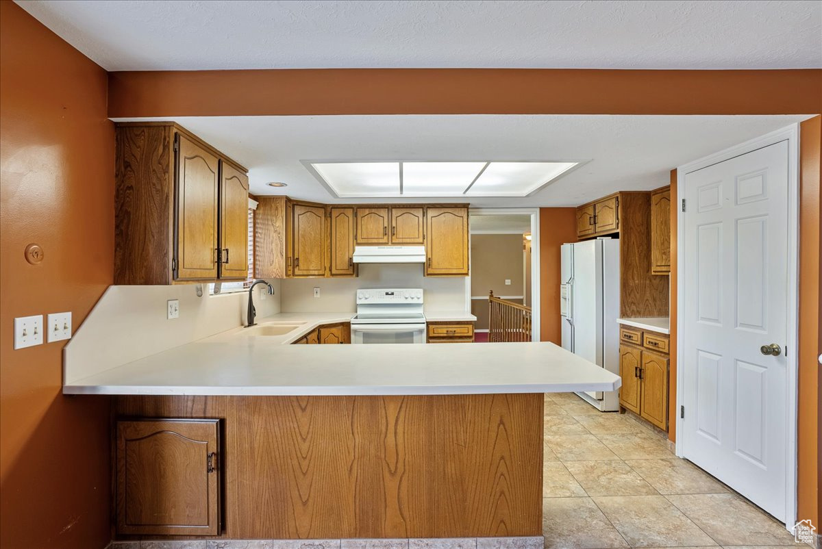 Kitchen featuring sink, kitchen peninsula, white appliances, and light tile patterned floors