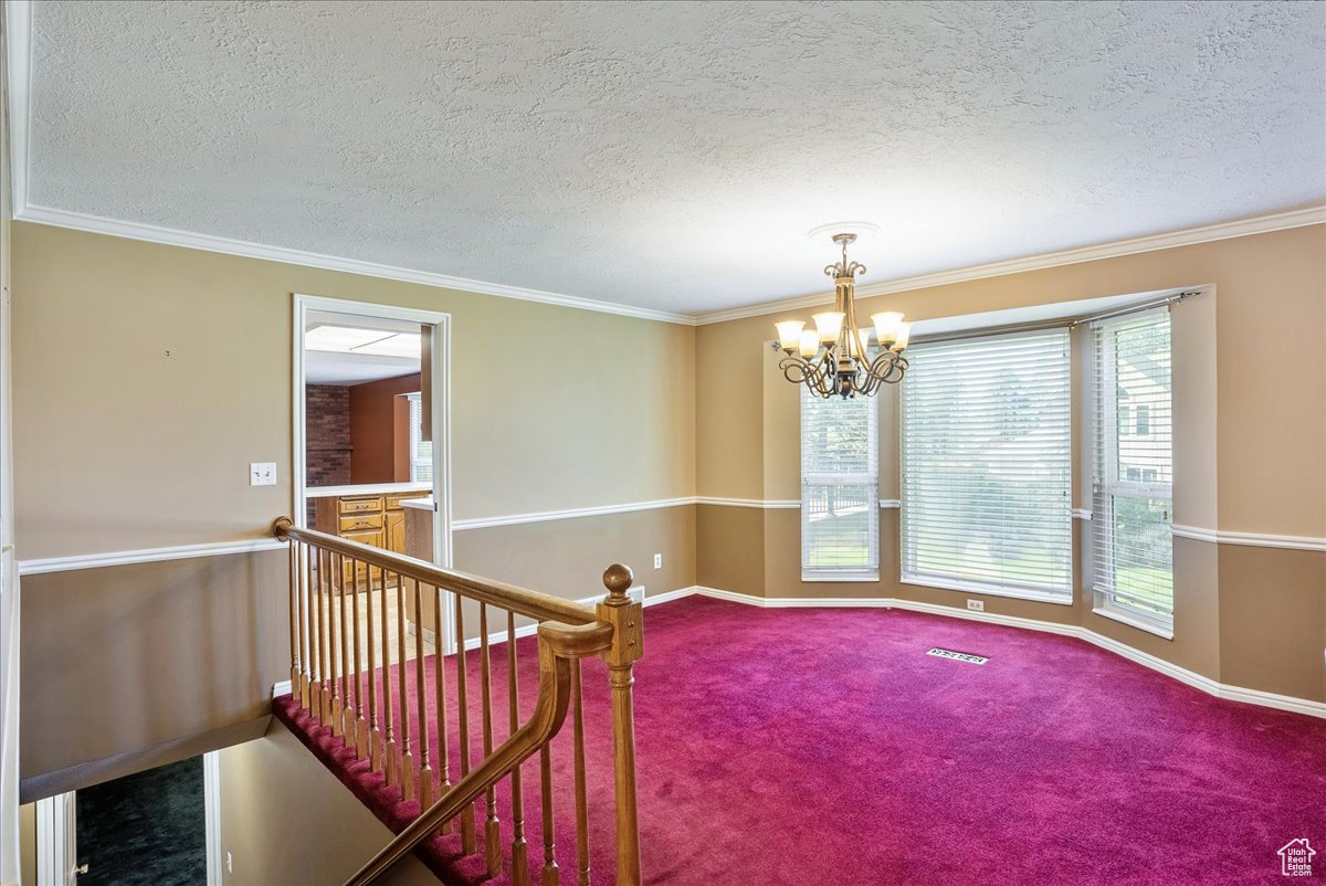 Unfurnished room featuring carpet, a textured ceiling, and an inviting chandelier