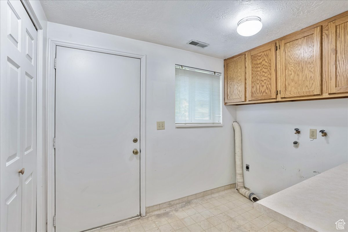 Clothes washing area with hookup for an electric dryer, a textured ceiling, and cabinets