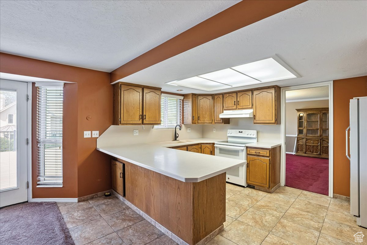 Kitchen featuring kitchen peninsula, light tile patterned floors, a textured ceiling, sink, and white appliances