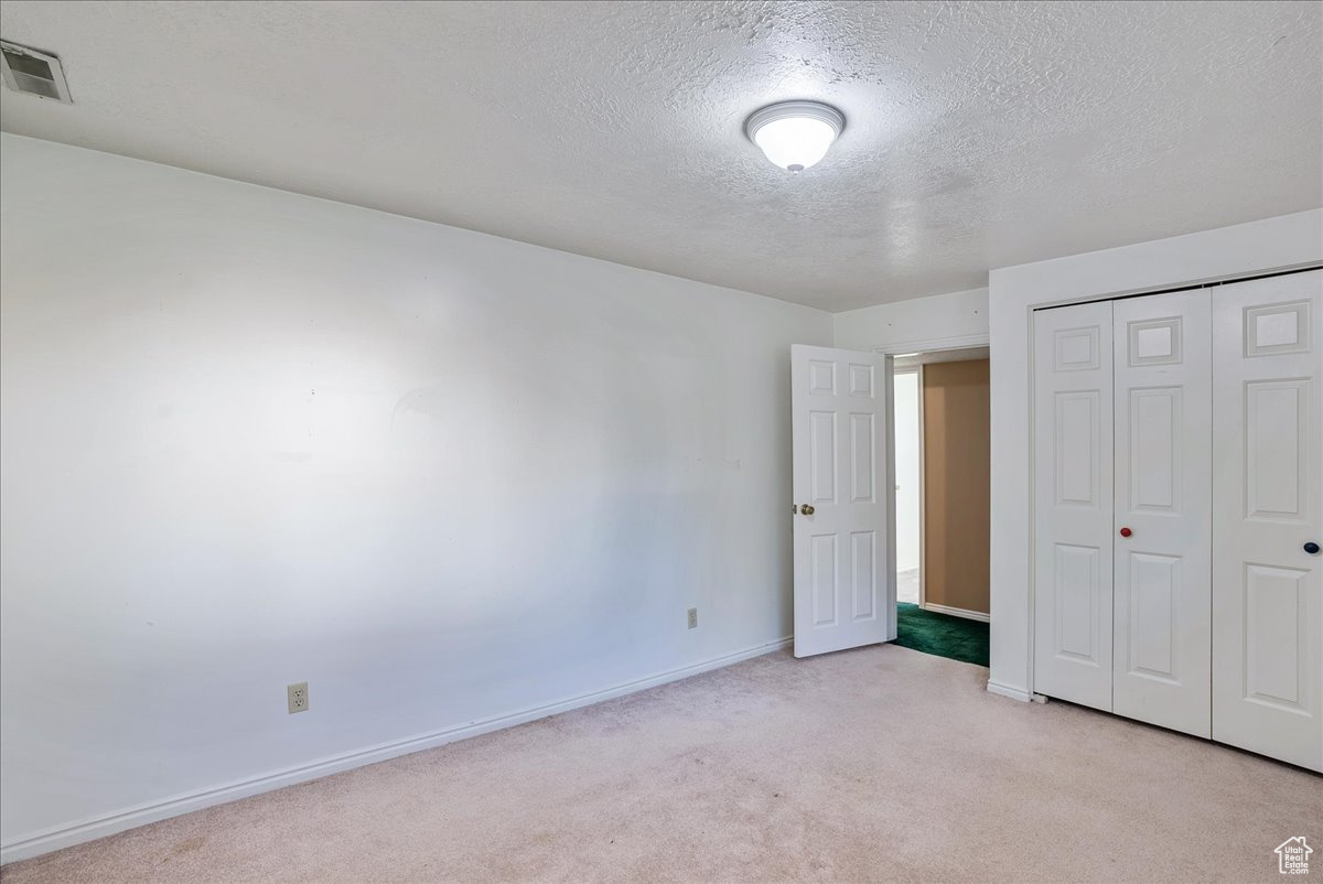 Unfurnished bedroom with a textured ceiling, light colored carpet, and a closet