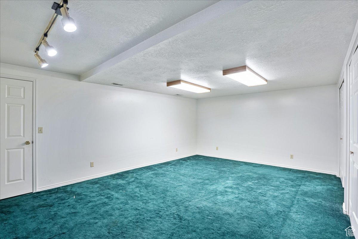 Carpeted spare room featuring beam ceiling, track lighting, and a textured ceiling