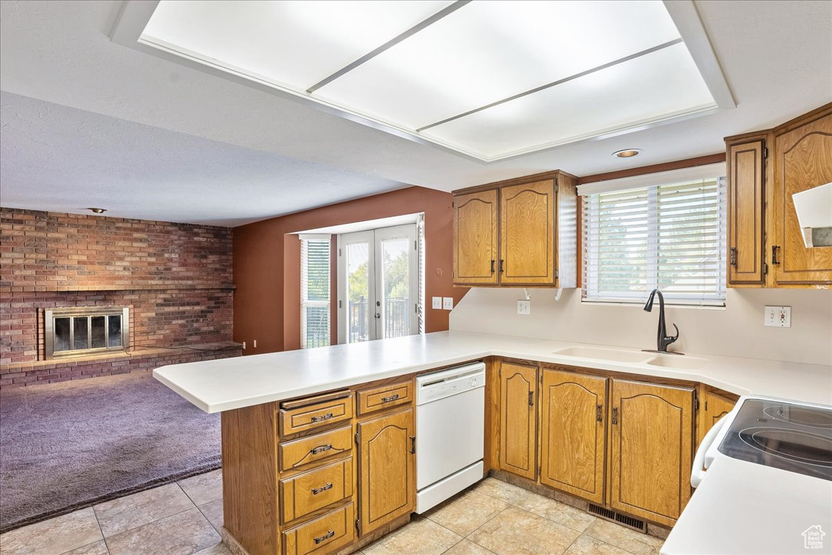 Kitchen with sink, light tile patterned flooring, dishwasher, a fireplace, and kitchen peninsula