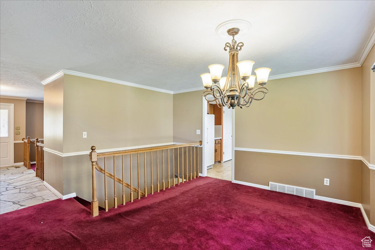 Carpeted spare room with ornamental molding, a notable chandelier, and a textured ceiling