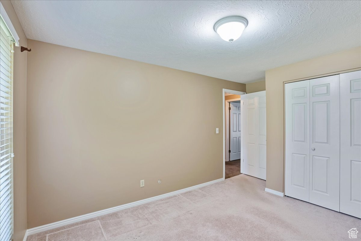 Unfurnished bedroom with a closet, a textured ceiling, and light colored carpet