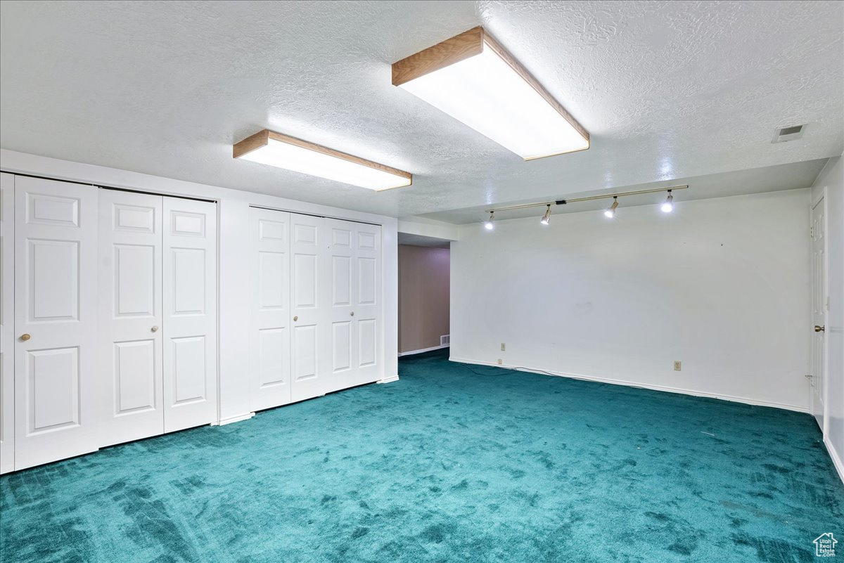 Basement featuring a textured ceiling, track lighting, and dark colored carpet