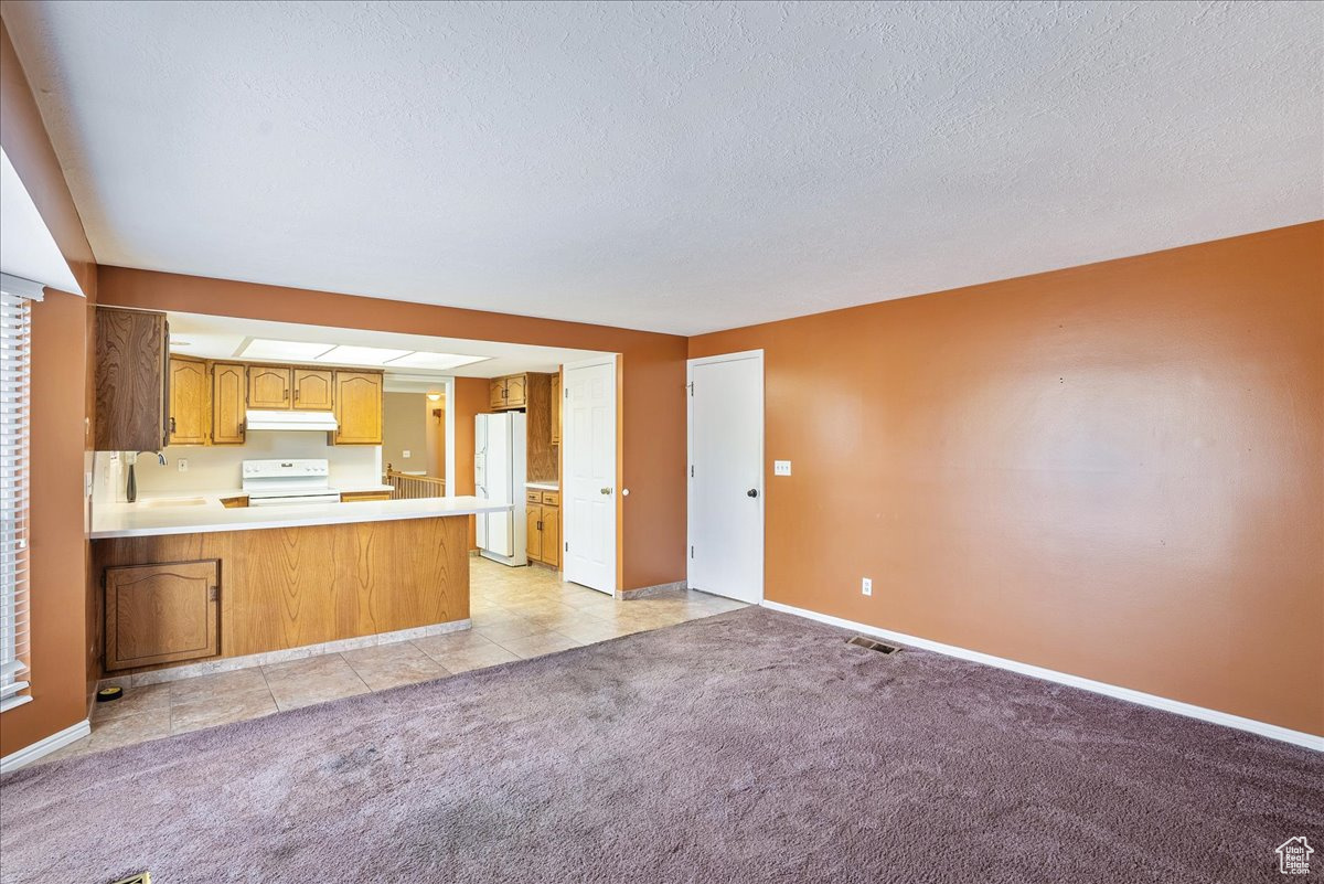 Kitchen featuring white appliances, sink, a textured ceiling, kitchen peninsula, and light carpet