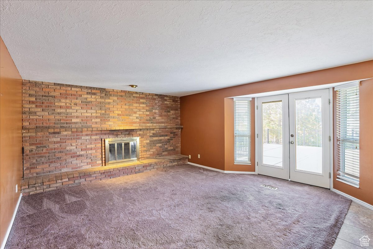 Unfurnished living room with french doors, a textured ceiling, a fireplace, and carpet floors