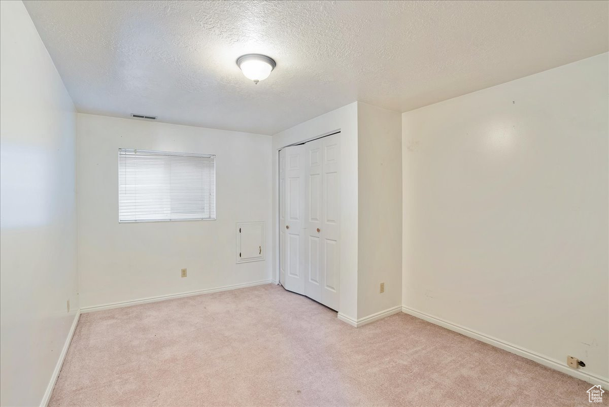 Unfurnished bedroom with light carpet, a textured ceiling, and a closet