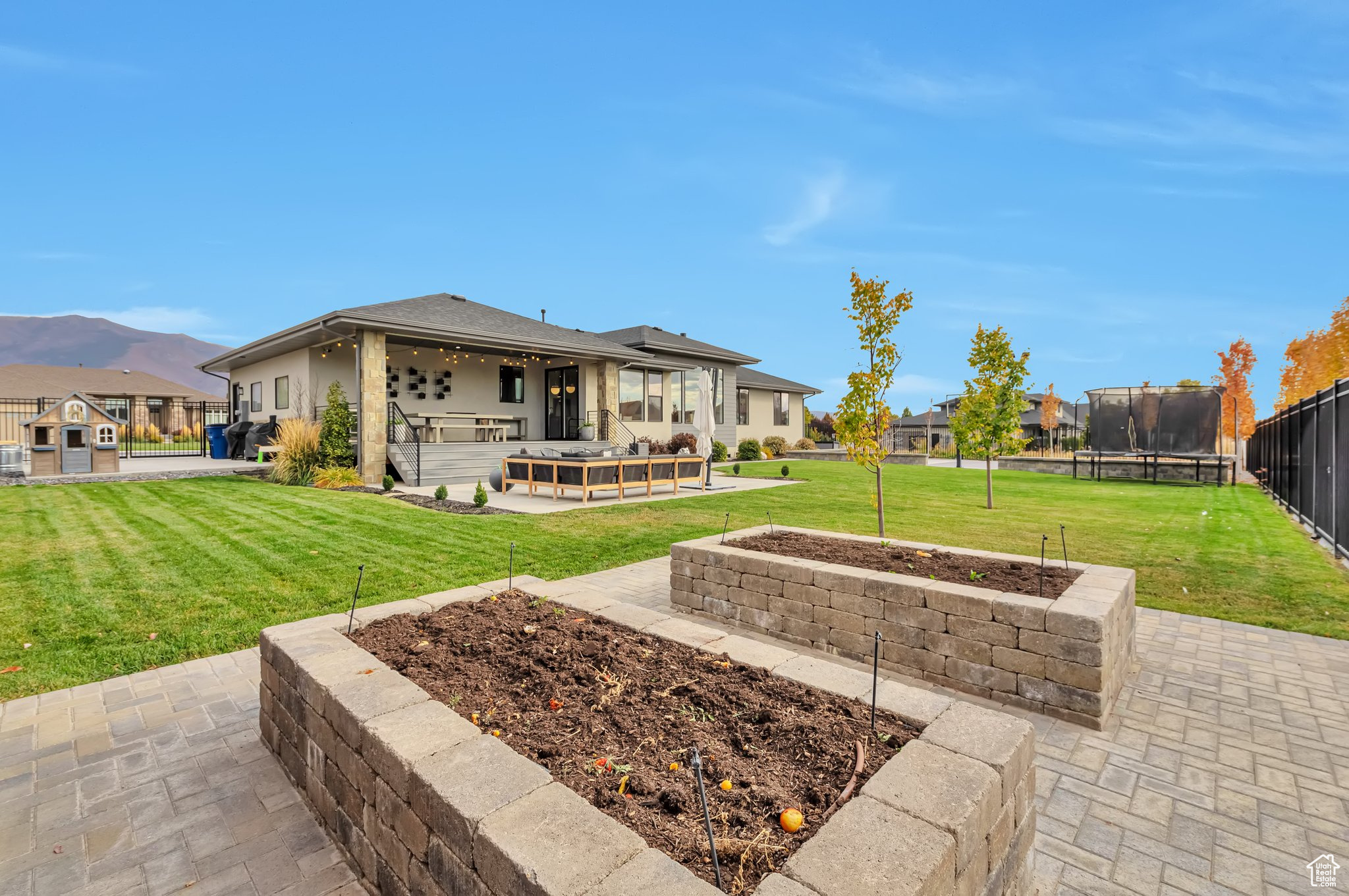 Rear view of house with a mountain view, a trampoline, a patio, and a lawn