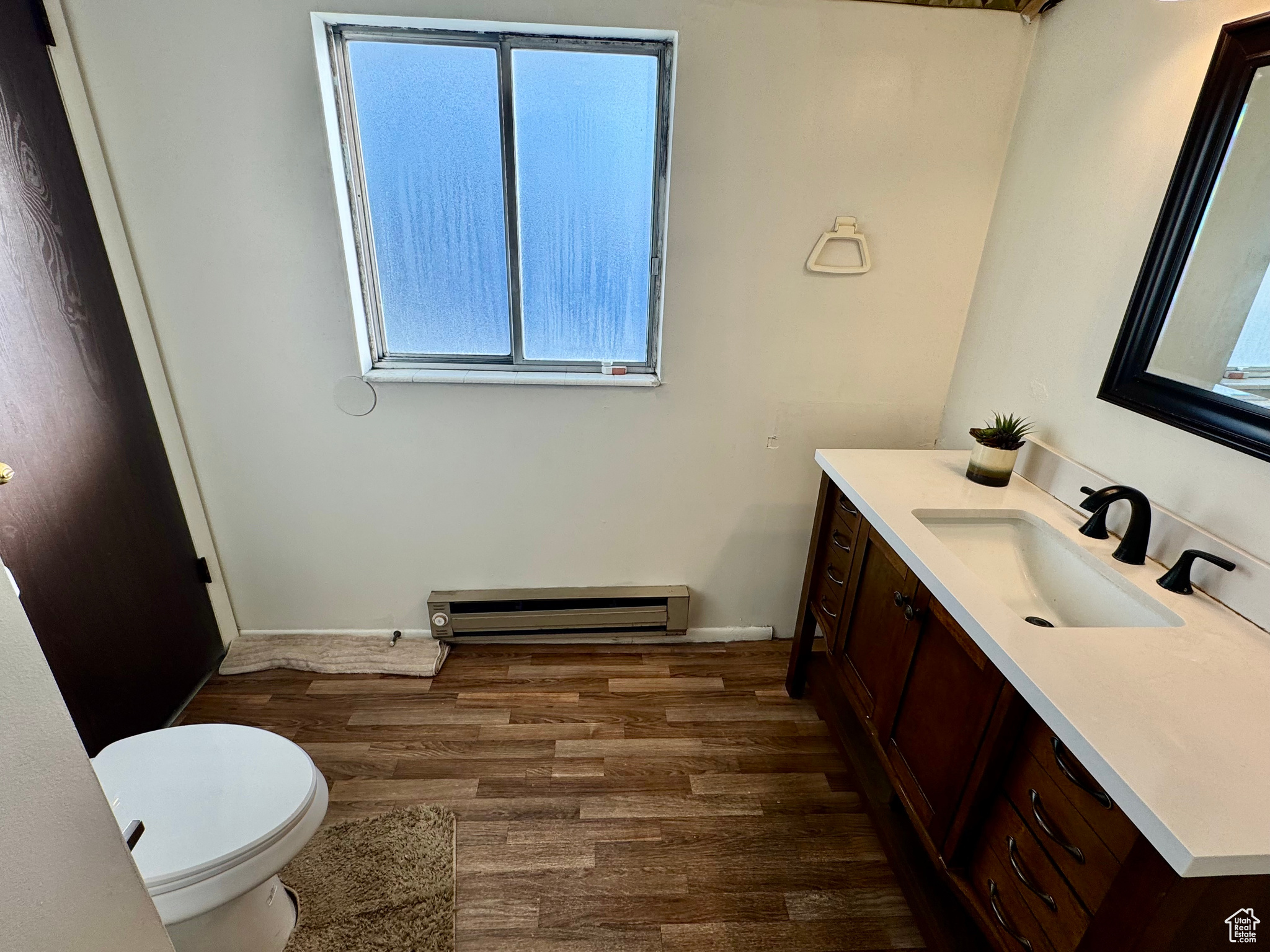 Bathroom with a wealth of natural light, vanity, baseboard heating, and hardwood / wood-style floors