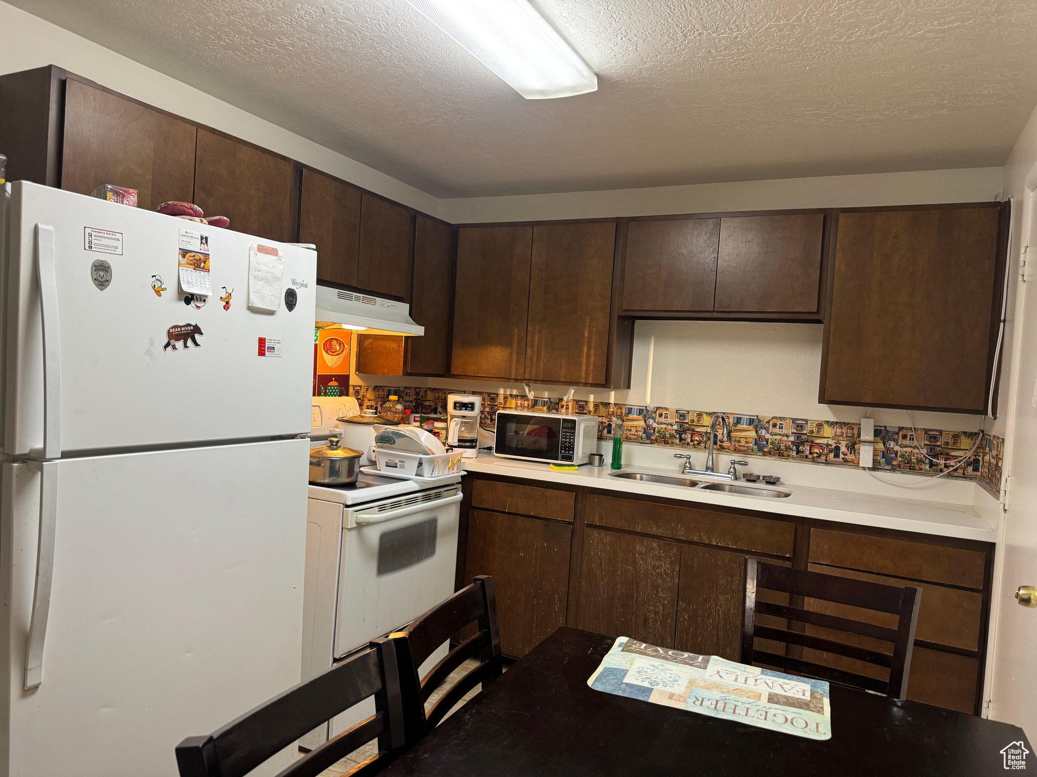 Kitchen with a textured ceiling, dark brown cabinets, sink, and white appliances