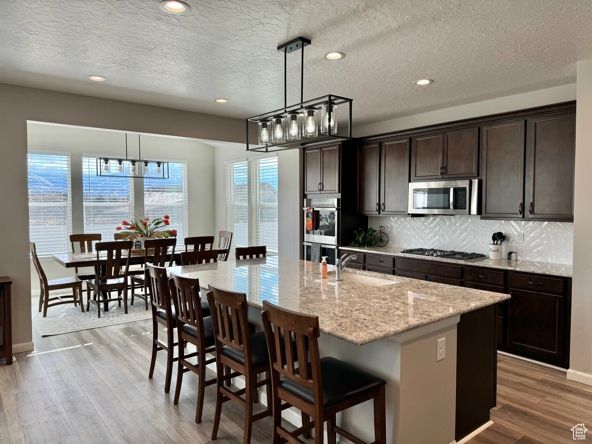 Gourmet Kitchen featuring an island with sink, decorative light fixtures, light wood-type flooring, and appliances with stainless steel finishes