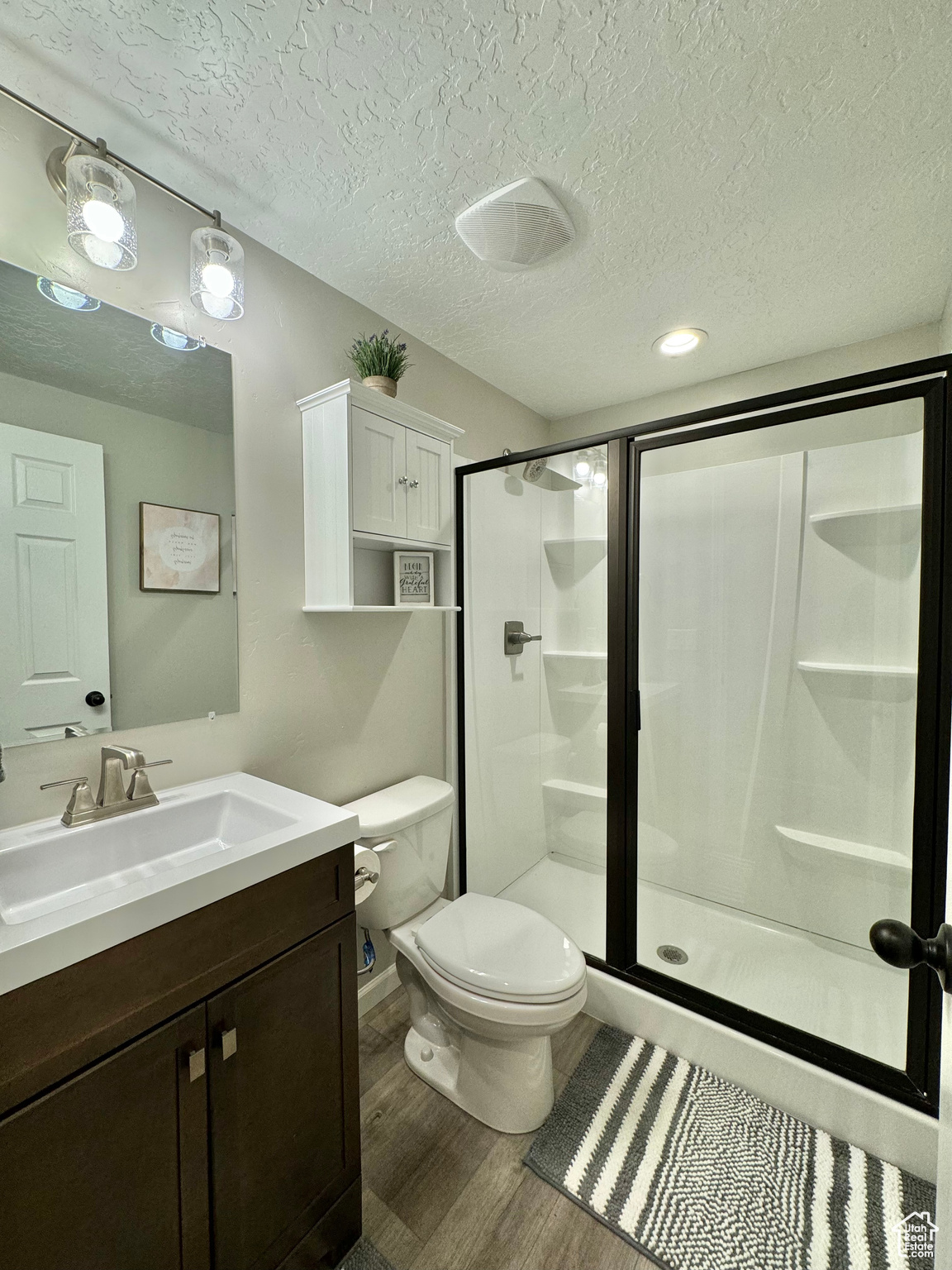 Basement Full Bathroom with a shower door, wood-type flooring, a textured ceiling, toilet, and vanity