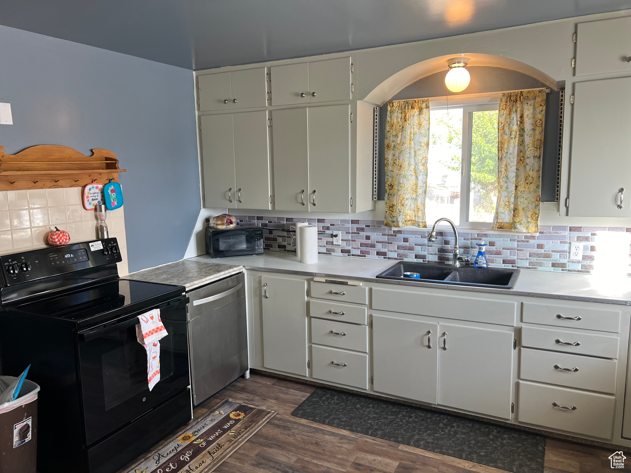 Kitchen with black appliances, sink, white cabinetry, decorative backsplash, and dark hardwood / wood-style floors