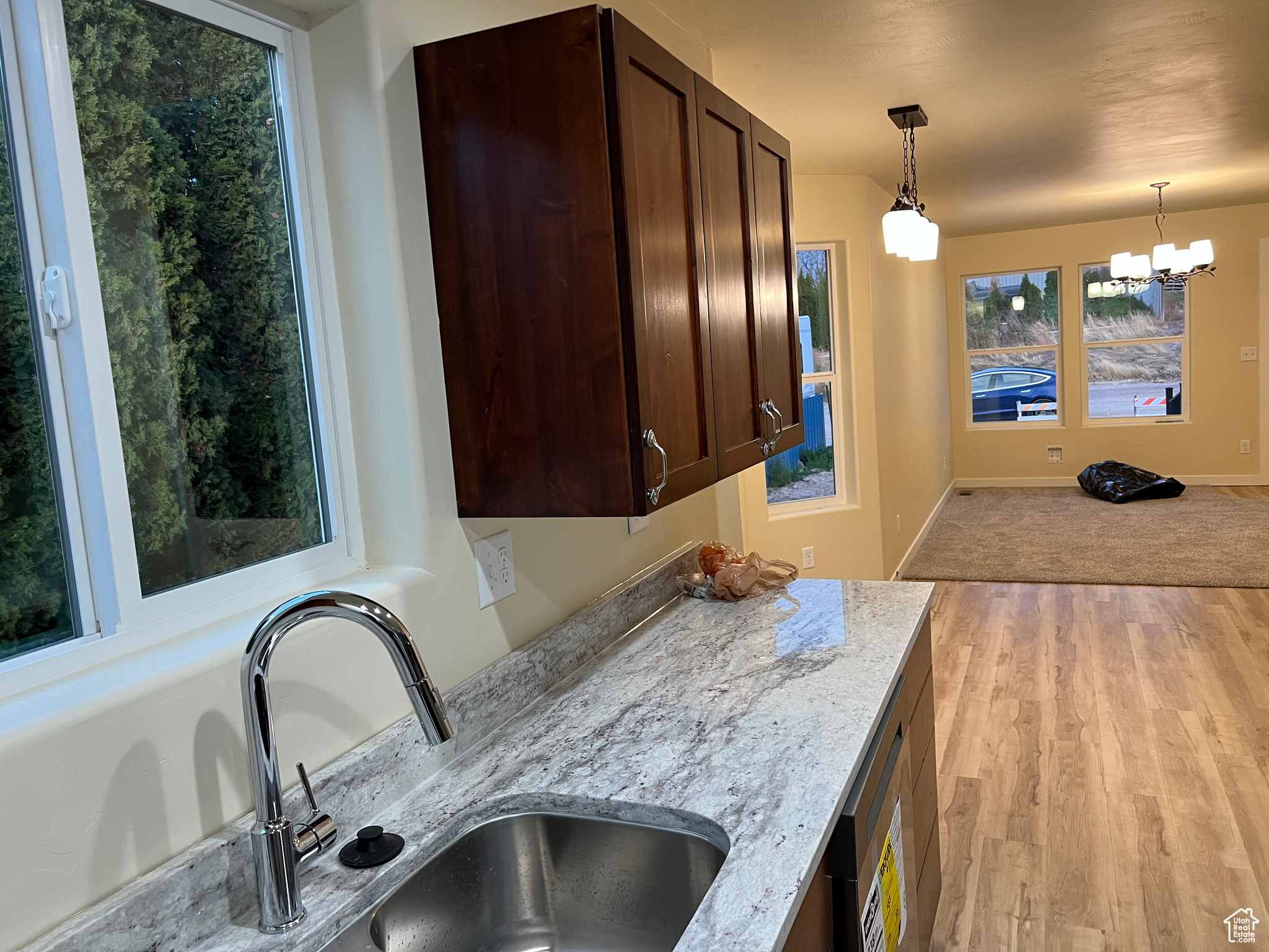 Kitchen with sink, hanging light fixtures, light stone counters, light hardwood / wood-style flooring, and a chandelier