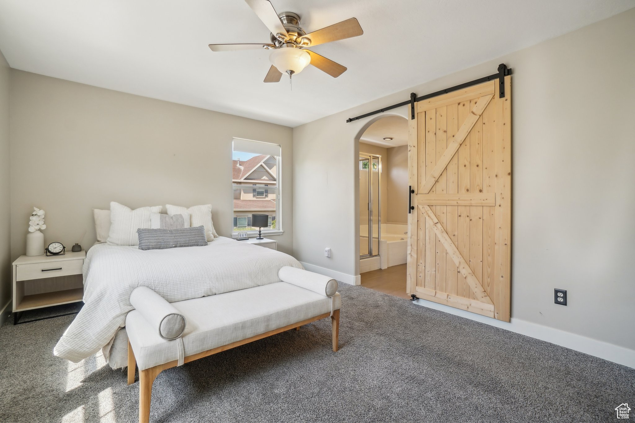 Carpeted bedroom with ensuite bathroom, a barn door, and ceiling fan