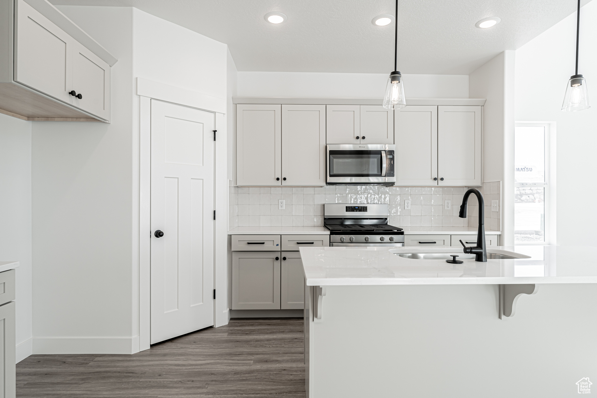 Kitchen featuring light countertops, decorative backsplash, appliances with stainless steel finishes, wood finished floors, and a sink