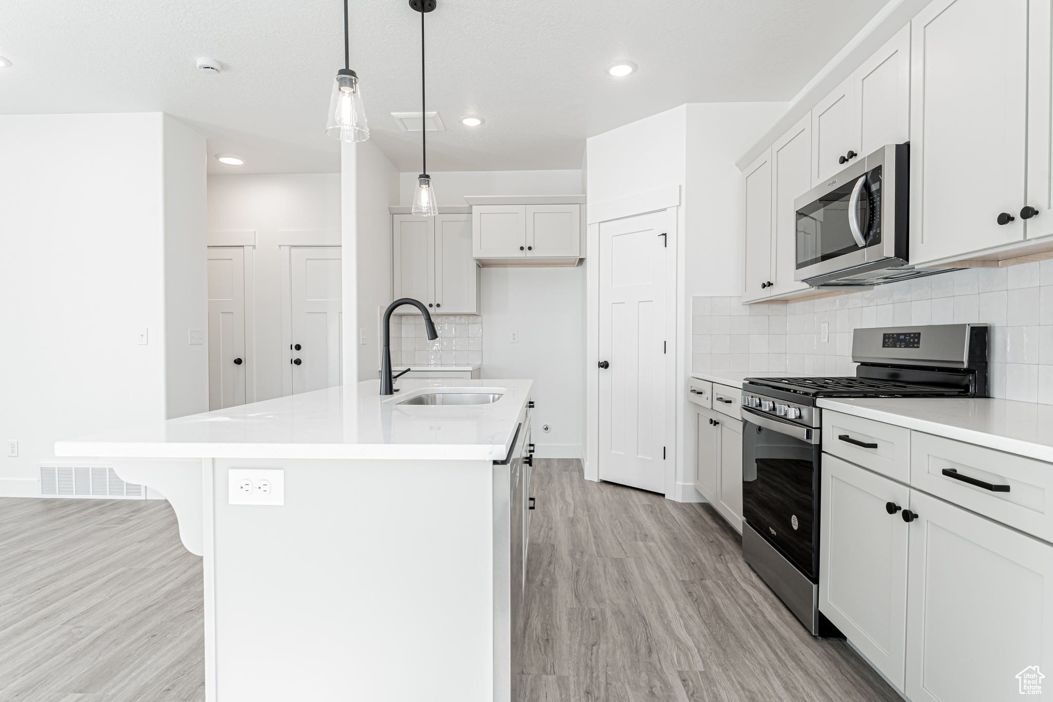 Kitchen featuring a center island with sink, stainless steel appliances, light wood-type flooring, and a sink