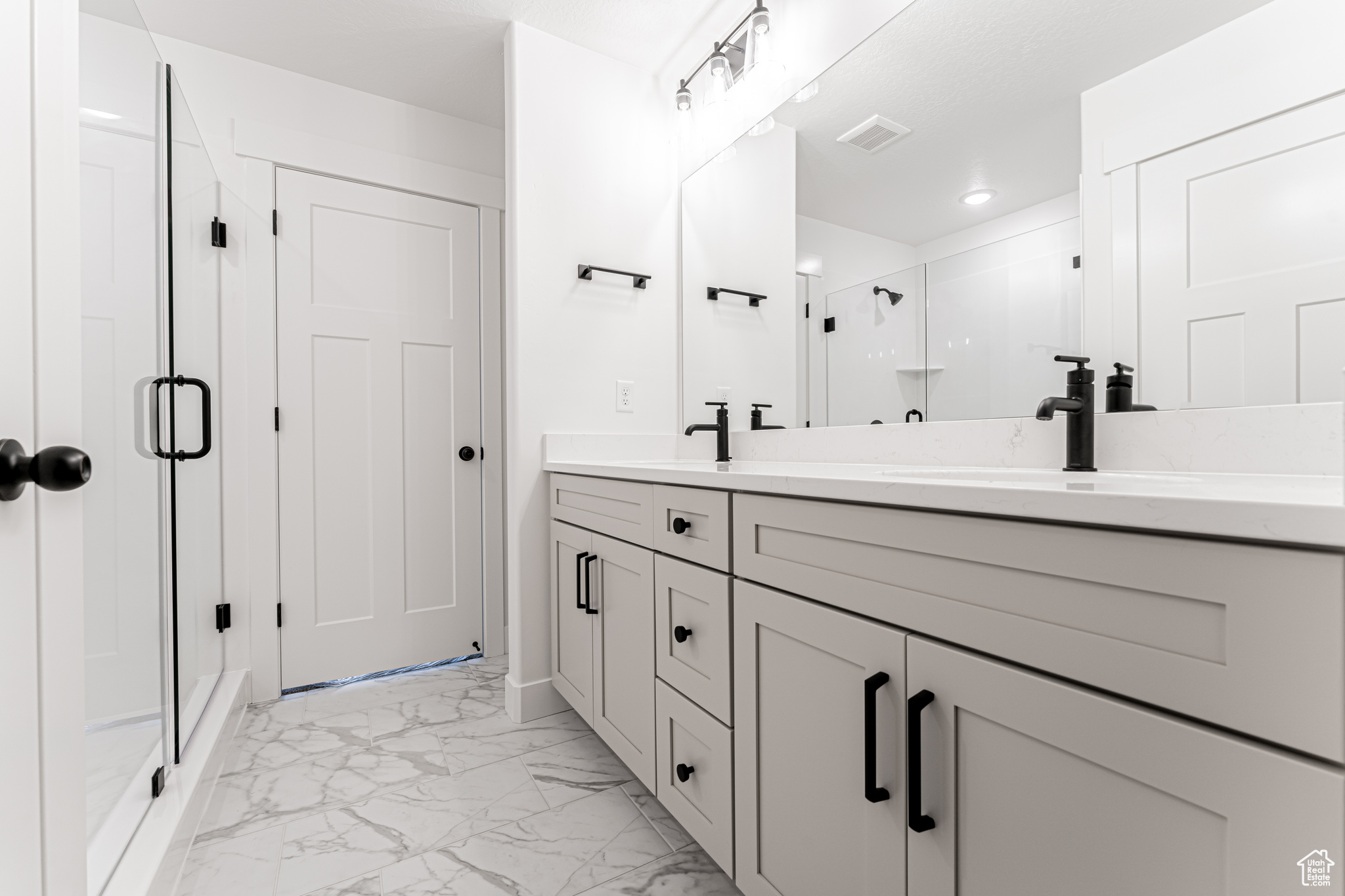 Bathroom featuring visible vents, double vanity, a sink, a shower stall, and marble finish floor